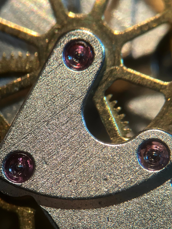 Это мост ангренажа - главная колесная система. И тут виден меткий мусор, а бушоны (розовые рубиновые камни, выполняющие роль подшипников) имеют загрязнения в виде старой смазки и результатов трения