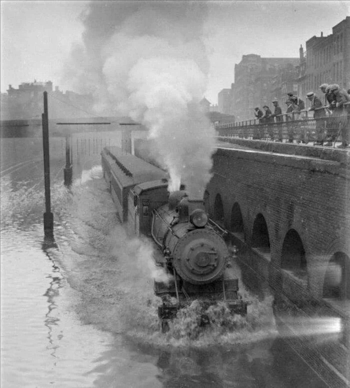 A steam locomotive moves through a flooded street during the Boston flood, 1915 - The photo, Black and white photo, Boston, 1915, Locomotive