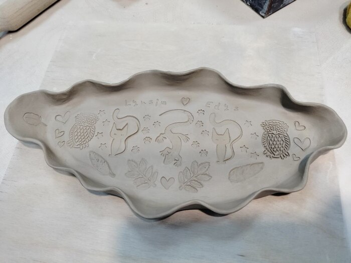 Тарелка из глины. Селедочница овальной формы с волнистыми краями, внутри штампами сделаны рисунки сов, котов, ящерицы, перьев и листиков растений.