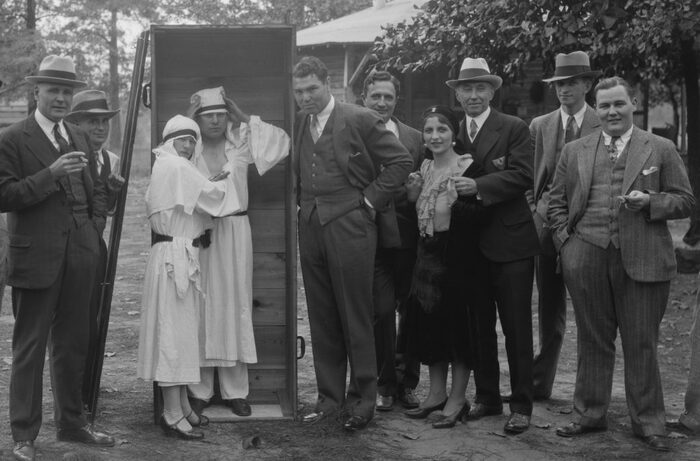 Лилли Мей Фолк в окружении мужчин: ее обнимает неизвестный господин в шляпе, слева — боксер Джек Демпси, возле ящика в белых одеждах — факир «Великий Паша» Уильям Карриган и его ассистентка Мадам Флозель.