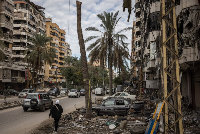 A woman walks past buildings and palm trees damaged by Israeli airstrikes on Hadi Nasrallah Street, which goes through a Beirut suburb, Dahiyeh, in Lebanon on Friday. (Ed Ram)