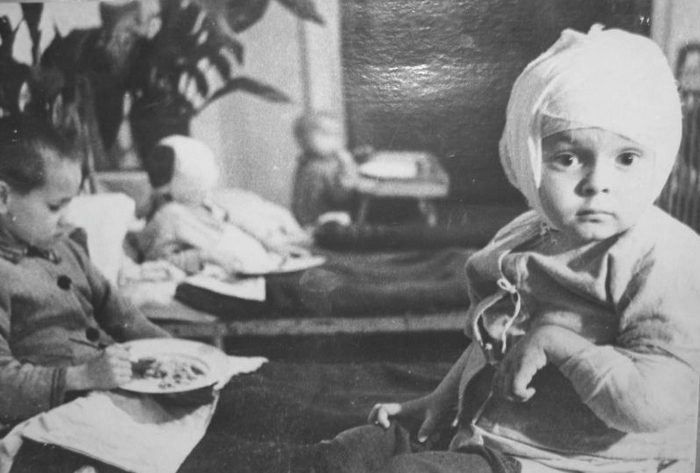 Ленинградские дети, раненные при артиллерийских обстрелах города, в больнице во время обеда. На переднем плане — четырехлетний Геня Микулинас. Осколками немецкого снаряда его ранило в голову и левую руку
