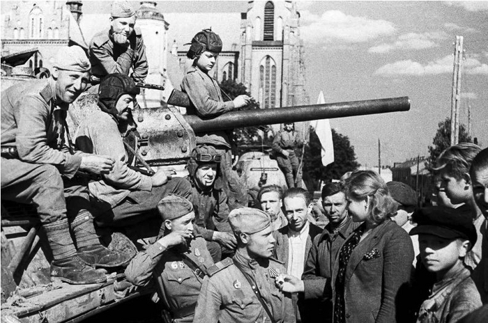 Жители освобожденного Белостока общаются с советскими танкистами и бойцами пехоты. Девушка осматривает орден Славы на гимнастерке сержанта. За танками Т-34 виден костел Успения девы Марии. В конце сентября 1944 года Белосток был включен в состав Польши